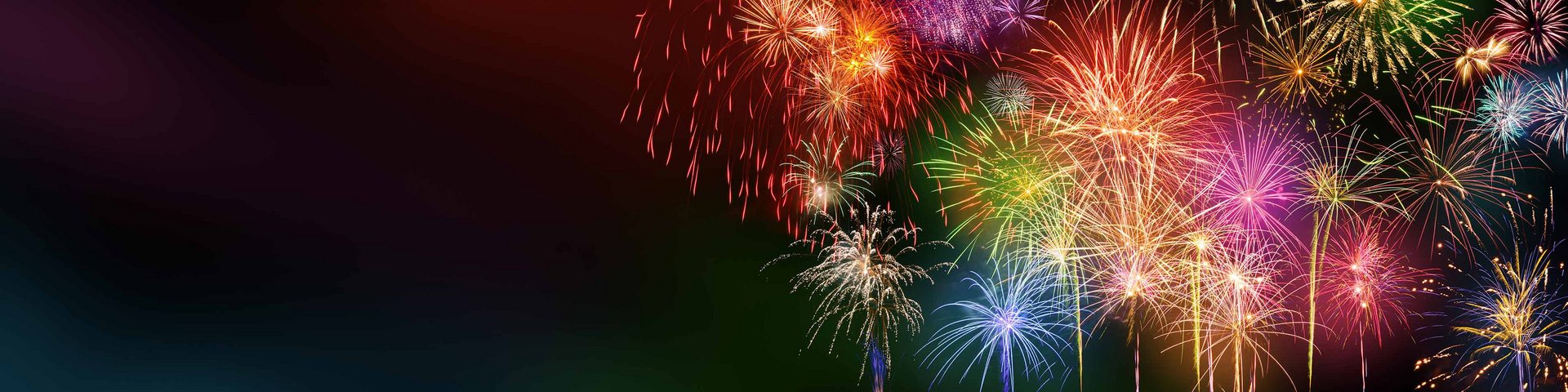 Farverige fyrværkerier eksploderer på nattehimlen, og skaber et festligt og glitrende syn. Lyskilderne udsender røde, grønne, blå og gule nuancer, der lyser op i mørket og fremkalder en fejring eller festlig anledning.